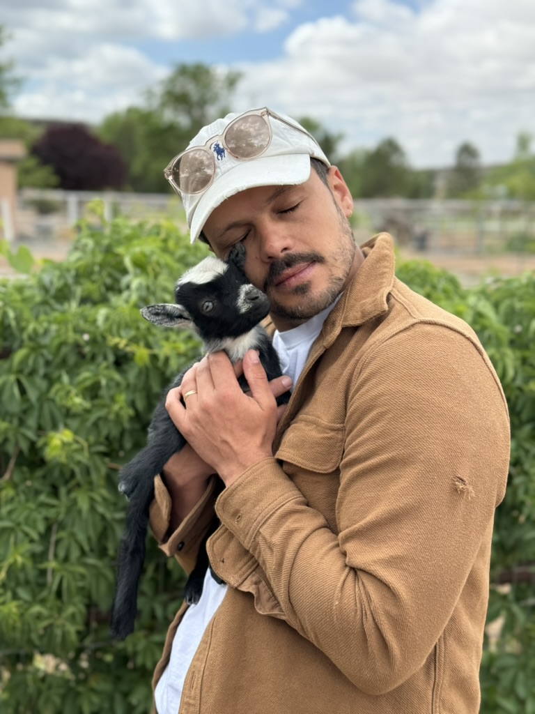 Kylan holding a baby goat in a green yard.